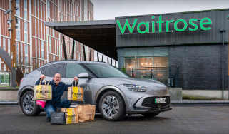 Auto Express chief sub-editor Andy Pringle crouching next to the Genesis GV60 while parked outside a Waitrose store