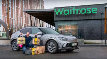 Auto Express chief sub-editor Andy Pringle crouching next to the Genesis GV60 while parked outside a Waitrose store