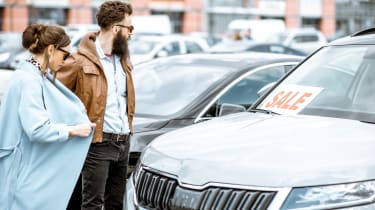 Two people browsing a car dealership forecourt