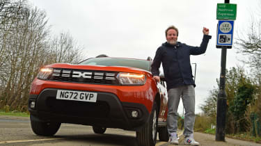 Auto Express web producer Pete Baiden standing next to the Dacia Duster and a ULEZ road sign