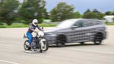 BMW X3 prototype (camouflaged) and dummy test car driving towards a motorcycle crash test dummy