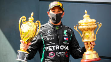 Lewis Hamilton sitting holding two trophies