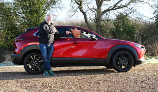 Auto Express executive editor Paul Adam standing next to the Mazda CX-30 and pointing at a horse mask