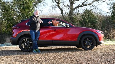 Auto Express executive editor Paul Adam standing next to the Mazda CX-30 and pointing at a horse mask