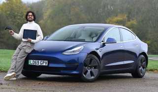 Auto Express senior staff writer Jordan Katsianis holding a laptop and leaning on a Tesla Model 3