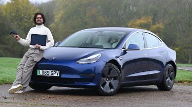 Auto Express senior staff writer Jordan Katsianis holding a laptop and leaning on a Tesla Model 3