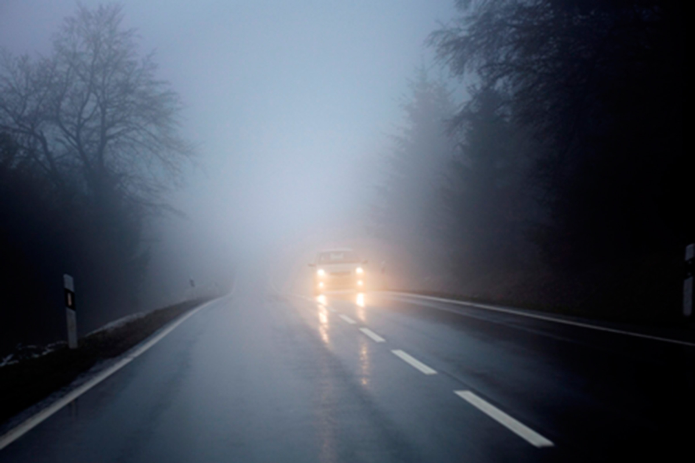 Car headlights piercing through dense fog