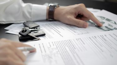 Person pointing at documents with car keys on top of them