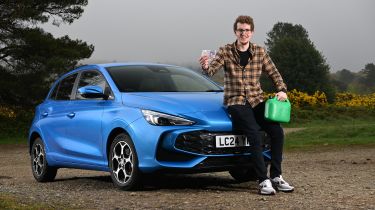 Auto Express content editor Ryan Birch sitting on the MG3&#039;s bonnet while holding a pound note and a gerry can