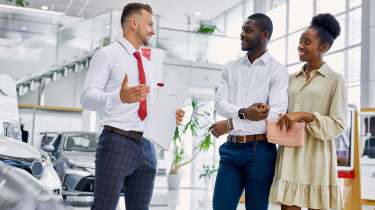 Two people talking to a salesperson in a car showroom