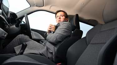 Auto Express consumer reporter Tom Jervis sitting in the Suzuki Swift while holding a cup of coffee