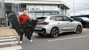 Auto Express news reporter Ellis Hyde holding two BMW iX1 undertrays
