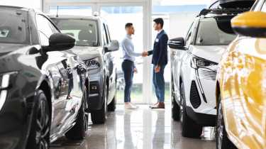 Two people shaking hands in between a collection of cars