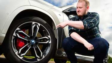 Auto Express news reporter Ellis Hyde leaning pointing at the BMW iX1&#039;s wheel