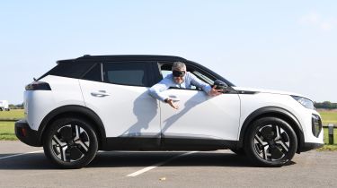 Auto Express deputy editor Richard Ingram leaning out of the Peugeot E-2008 while wearing a blindfold