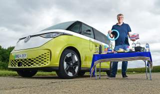 Auto Express editor Paul Barker standing next to the Volkswagen ID.Buzz with a table covered in various items