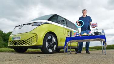 Auto Express editor Paul Barker standing next to the Volkswagen ID.Buzz with a table covered in various items